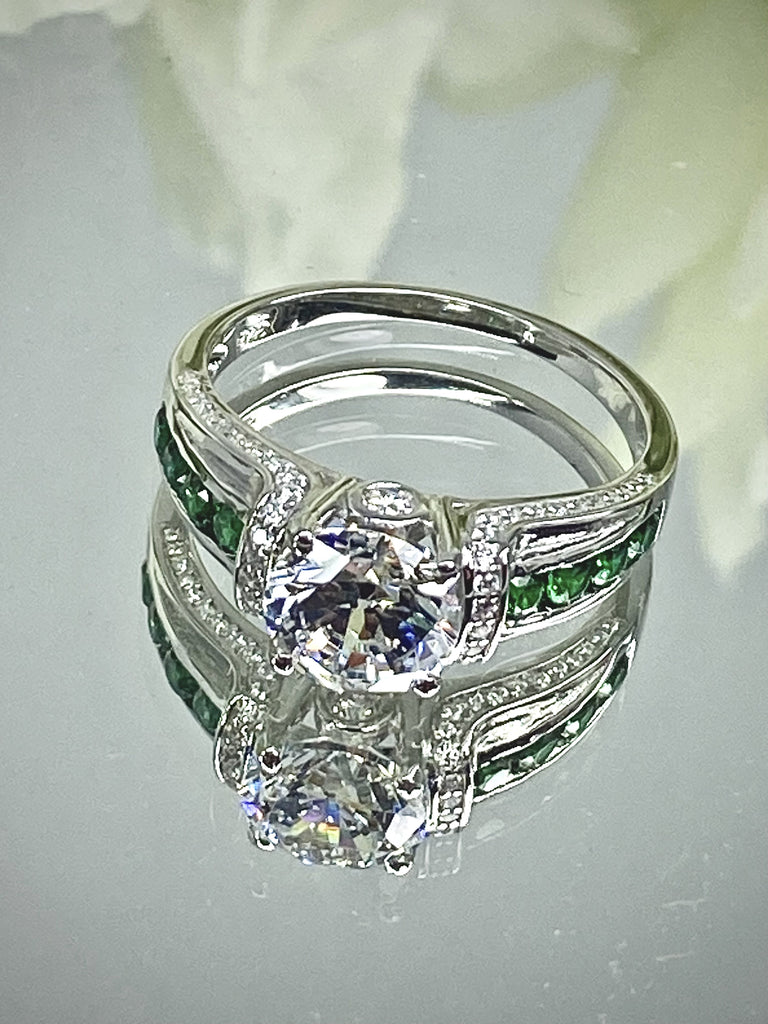 white CZ art deco ring, center stone is round cut white CZ, there are two trails of emerald green accents traveling up the sides of the band and two more trails of white CZs on each side of the band partially encircling the center stone, finally there are two accent white CZs on each of the remaining sides of the center stone; White CZ Ring with Emerald Accent gems, Art Deco Jewelry, Sterling silver Filigree, Silver Embrace Jewelry, D220 Deco Inlay