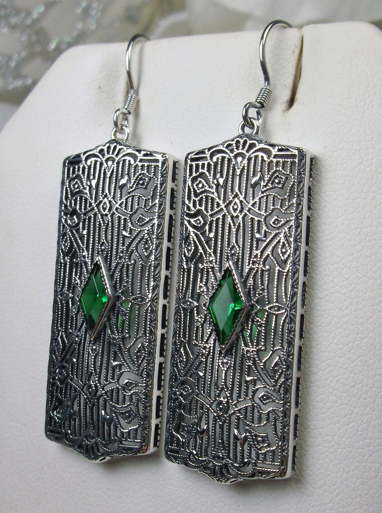 Rectangle Art Deco style earrings with fine lace filigree and a diamond shaped emerald green gemstone in the center of the lace filigree field, traditional shepherd hook style ear wire closures