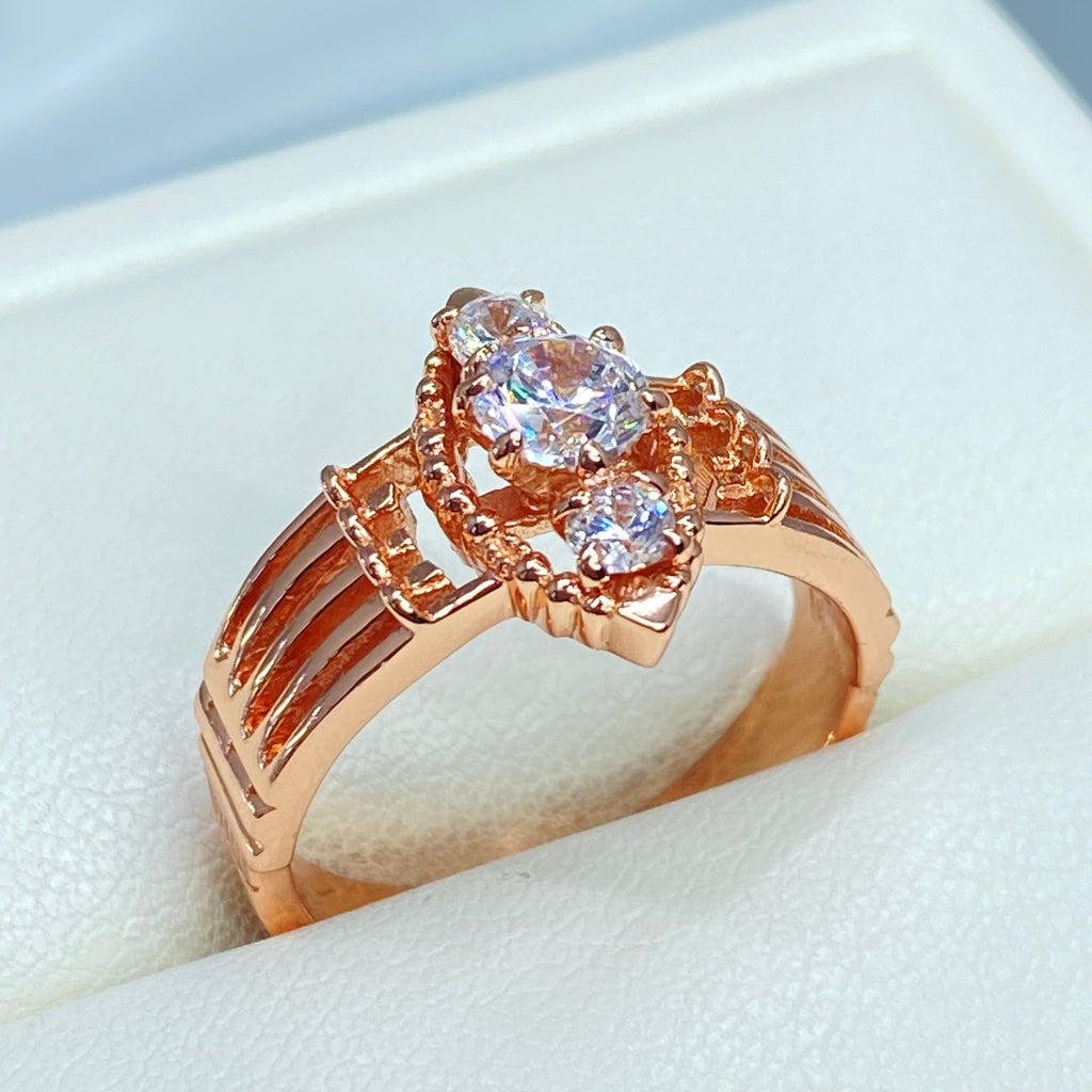Rose gold ring with multiple sparkling gems on a light background, a three stone ring with a White CZ center. Rose Gold plated Sterling Silver Art Deco Filigree, fine detail, Silver Embrace Jewelry, Xanadu D164