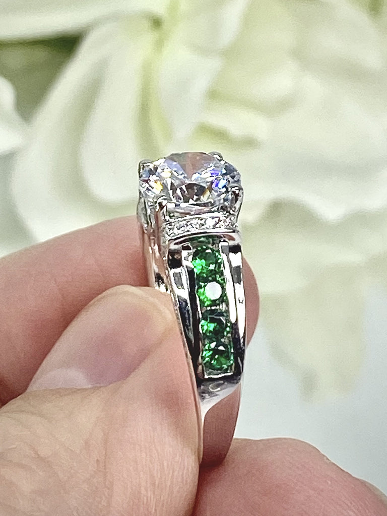 white CZ art deco ring, center stone is round cut white CZ, there are two trails of emerald green accents traveling up the sides of the band and two more trails of white CZs on each side of the band partially encircling the center stone, finally there are two accent white CZs on each of the remaining sides of the center stone; White CZ Ring with Emerald Accent gems, Art Deco Jewelry, Sterling silver Filigree, Silver Embrace Jewelry, D220 Deco Inlay