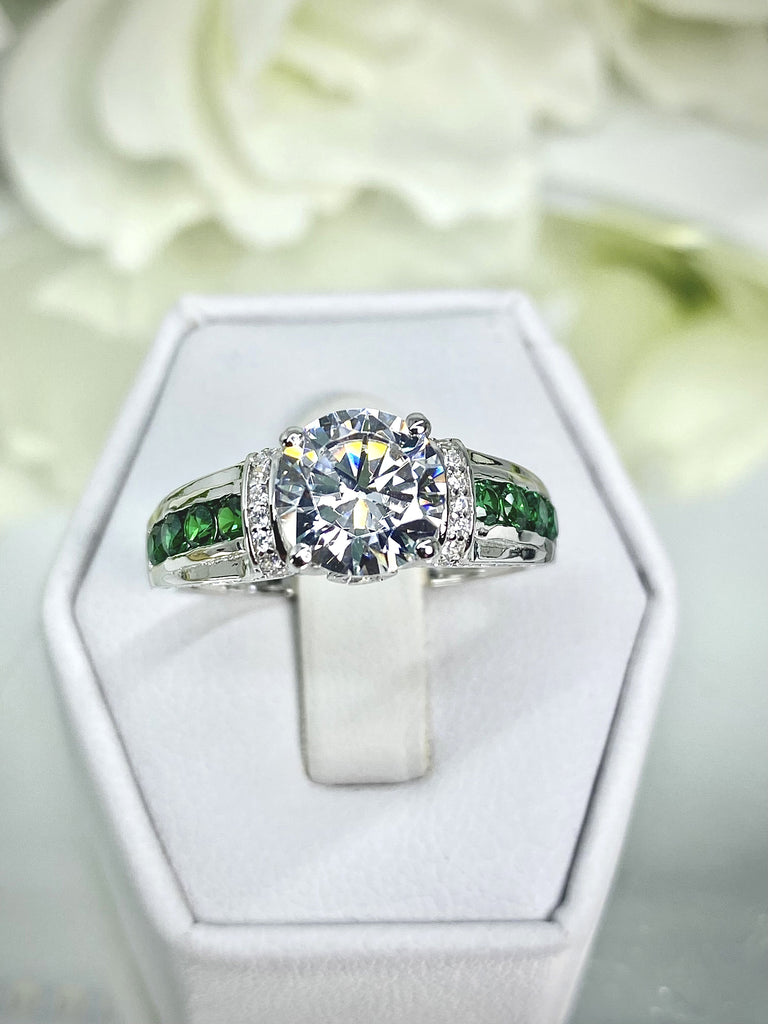 white CZ art deco ring, center stone is round cut white CZ, there are two trails of emerald green accents traveling up the sides of the band and two more trails of white CZs on each side of the band partially encircling the center stone, finally there are two accent white CZs on each of the remaining sides of the center stone; White CZ Ring with Emerald Accent gems, Art Deco Jewelry, Sterling silver Filigree, Silver Embrace Jewelry, D220 Deco Inlay