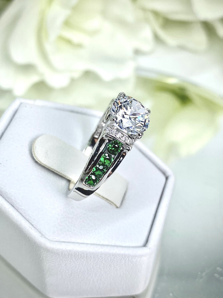 white CZ art deco ring, center stone is round cut white CZ, there are two trails of emerald green accents traveling up the sides of the band and two more trails of white CZs on each side of the band partially encircling the center stone, finally there are two accent white CZs on each of the remaining sides of the center stone; White CZ Ring with Emerald Accent gems, Art Deco Jewelry, Sterling silver Filigree, Silver Embrace Jewelry, D220 Deco Inlay