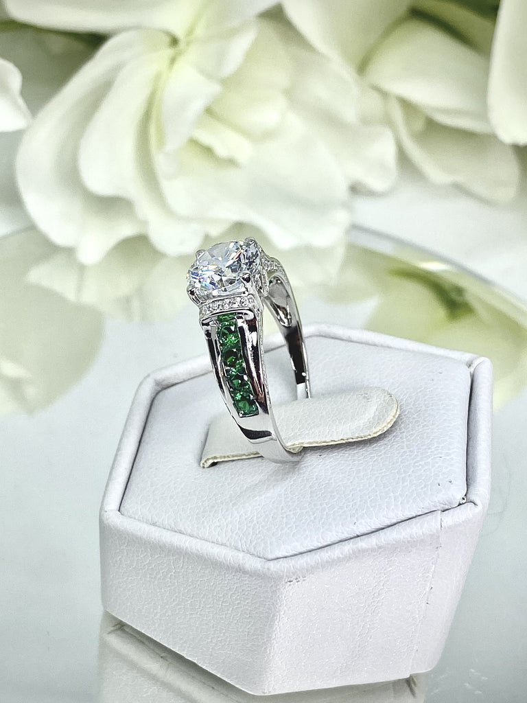 white CZ art deco ring, center stone is round cut white CZ, there are two trails of emerald green accents traveling up the sides of the band and two more trails of white CZs on each side of the band partially encircling the center stone, finally there are two accent white CZs on each of the remaining sides of the center stone; White CZ Ring with Emerald Accent gems, Art Deco Jewelry, Sterling silver Filigree, Silver Embrace Jewelry, D220 Deco Inlay