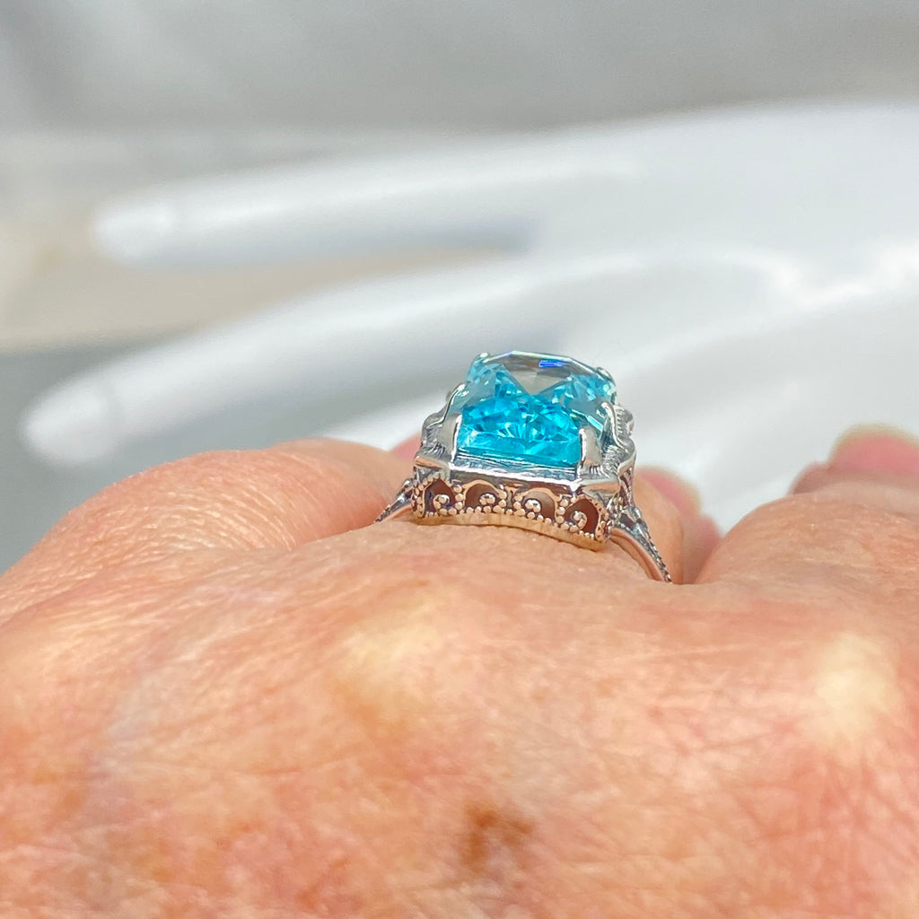 Simulated Aquamarine Ring, Edwardian Jewelry, Sterling silver filigree, Silver Embrace Jewelry D232, Aquamarine Ring with a blue gemstone on a finger against a blurred background