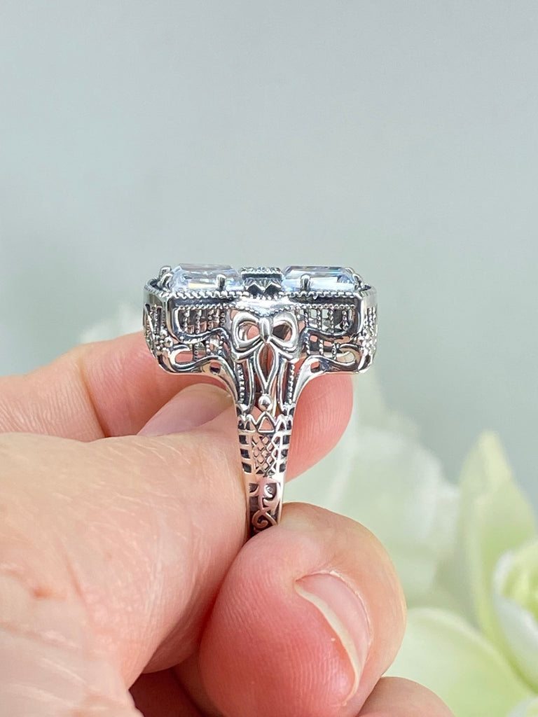 White CZ Ring, With Moissanite Inset gem in the center, Sterling Silver Filigree, Silver Embrace Jewelry, D595 Versailles Ring. A 925 sterling silver ring with four central CZ gems, adorned with a bow, a stone, petite blossoms and two bows on the band. The ring showcases French/Baroque style with meticulous detailing.
