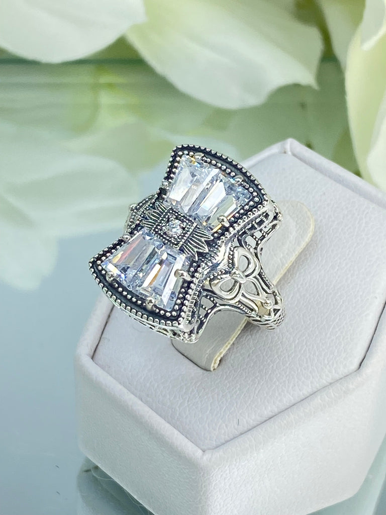 White CZ Ring, With Moissanite Inset gem in the center, Sterling Silver Filigree, Silver Embrace Jewelry, D595 Versailles Ring. A 925 sterling silver ring with four central CZ gems, adorned with a bow, a stone, petite blossoms and two bows on the band. The ring showcases French/Baroque style with meticulous detailing.