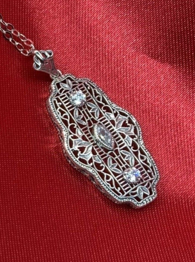white CZ art deco pendant, center stone is marquise cut white CZ, there are two white CZs above and below the center stone, delicate floral filigree surrounds all stones and edges the sides of the pendant