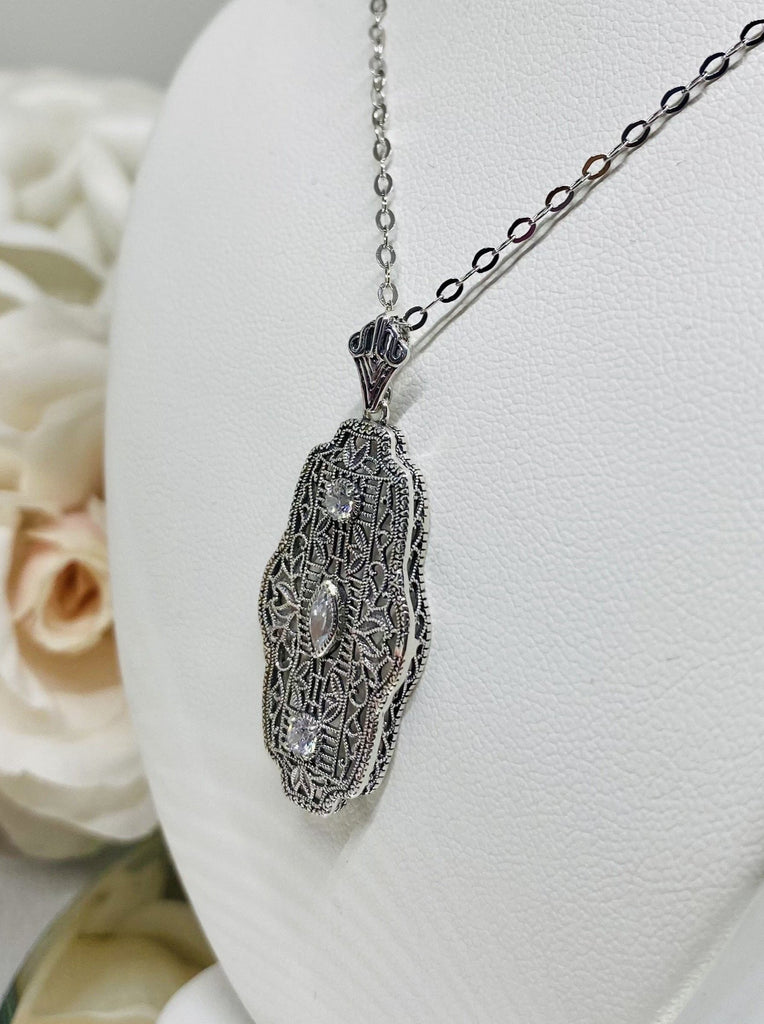 white CZ art deco pendant, center stone is marquise cut white CZ,  there are two white CZs above and below the center stone, delicate floral filigree surrounds all stones and edges the sides of the pendant
