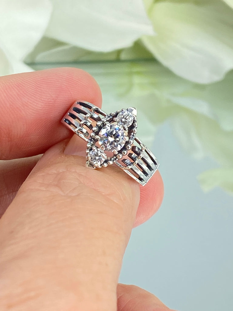 a close up of a person holding a ring a three stone ring with a White CZ center. Sterling Silver Art Deco Filigree, fine detail, Silver Embrace Jewelry, Xanadu D164