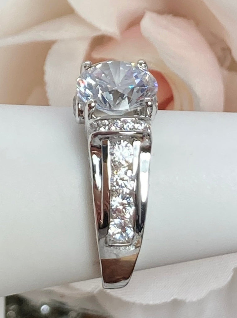 white CZ art deco ring, center stone is round cut white Cubic Zirconia, there are two trails of white CZ accents traveling up the sides of the band and two more trails of white CZs on each side of the band partially encircling the center stone, finally there are two accent white CZs on each of the remaining sides of the center stone
