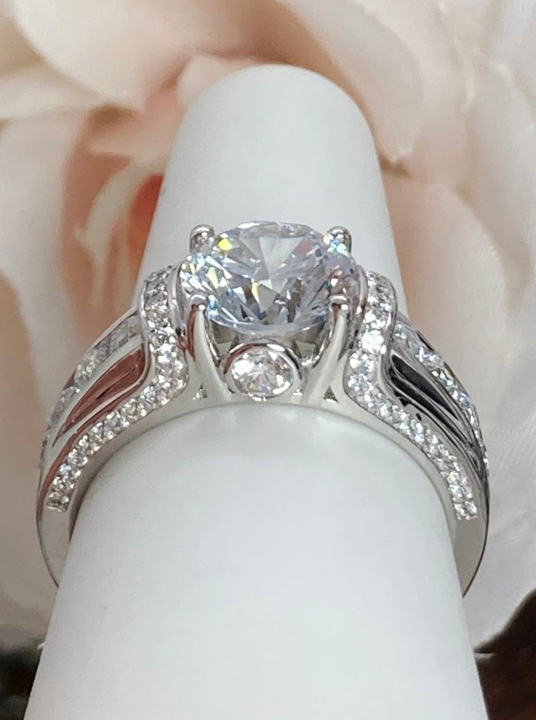 white CZ art deco ring, center stone is round cut white Cubic Zirconia, there are two trails of white CZ accents traveling up the sides of the band and two more trails of white CZs on each side of the band partially encircling the center stone, finally there are two accent white CZs on each of the remaining sides of the center stone