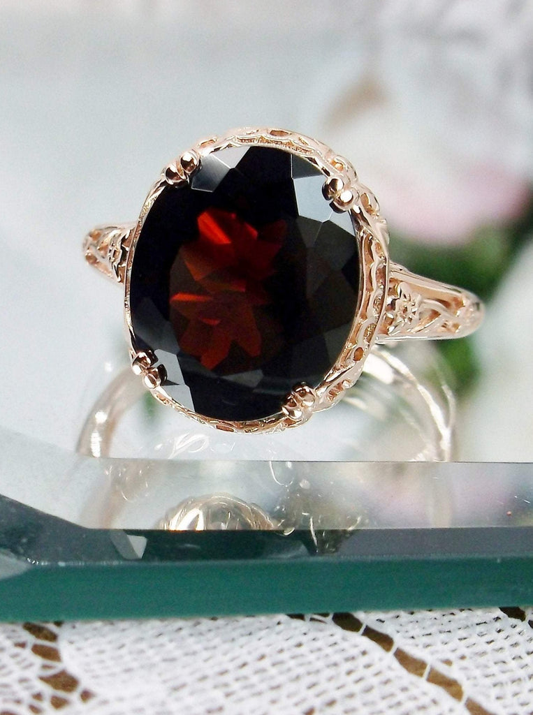 Natural Garnet Ring, Rose Gold over Sterling Silver, floral filigree setting and band, oval garnet stone, Edward design#70z, front view on a glass surface