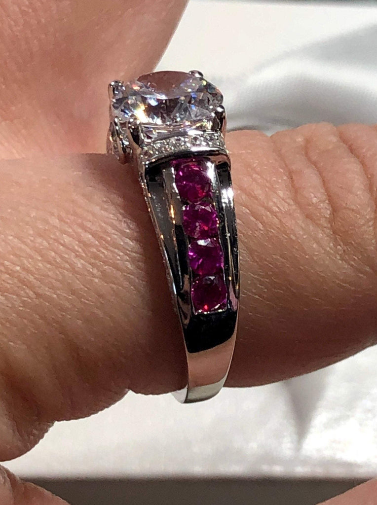 white CZ art deco ring, center stone is round cut white Cubic Zirconia, there are two trails of ruby red CZ accents traveling up the sides of the band and two more trails of white CZs on each side of the band partially encircling the center stone, finally there are two accent white CZs on each of the remaining sides of the center stone