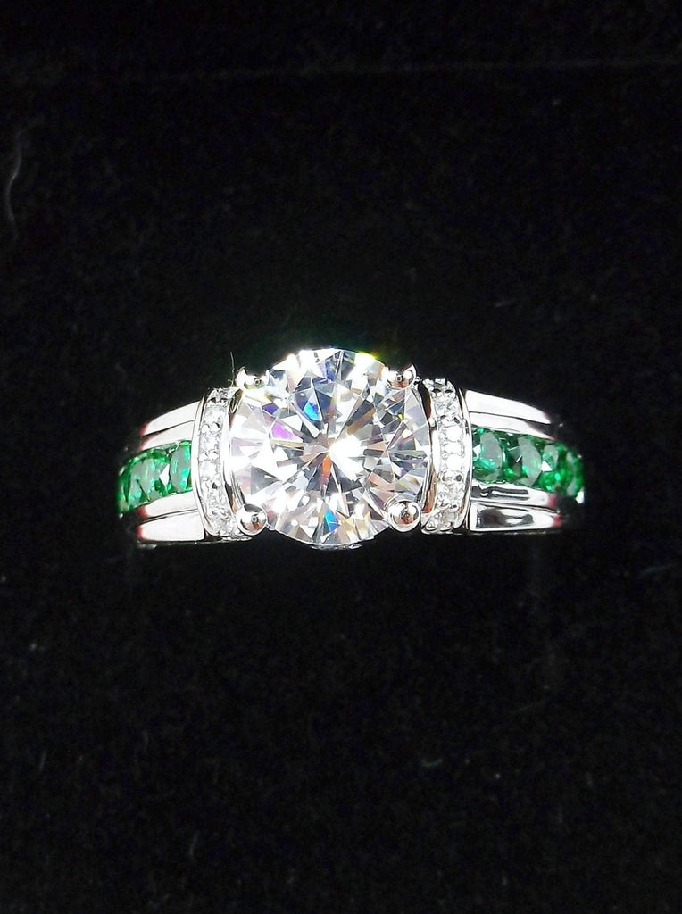 white CZ art deco ring, center stone is round cut white CZ, there are two trails of emerald green accents traveling up the sides of the band and two more trails of white CZs on each side of the band partially encircling the center stone, finally there are two accent white CZs on each of the remaining sides of the center stone